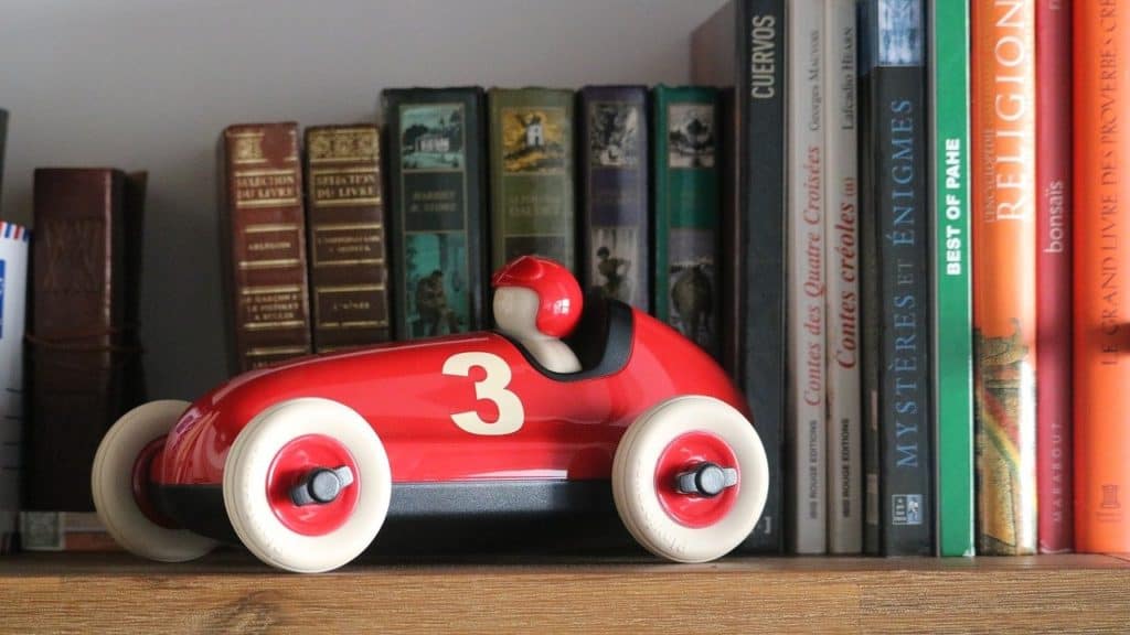 Red toy racing car on bookshelf in front of books