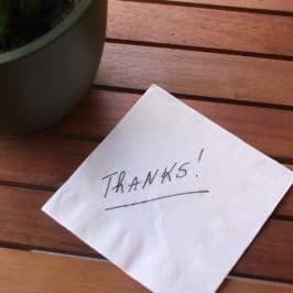 The word 'thanks' written on a napkin on a wooden table