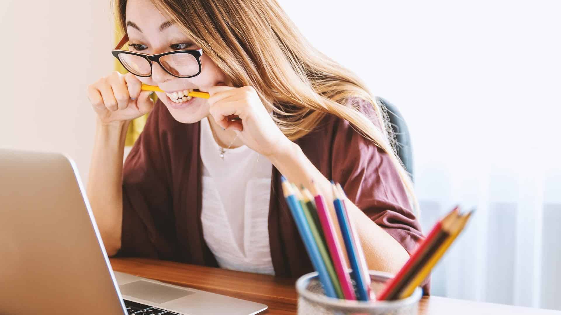 Woman biting pencil in frustration in front of laptop