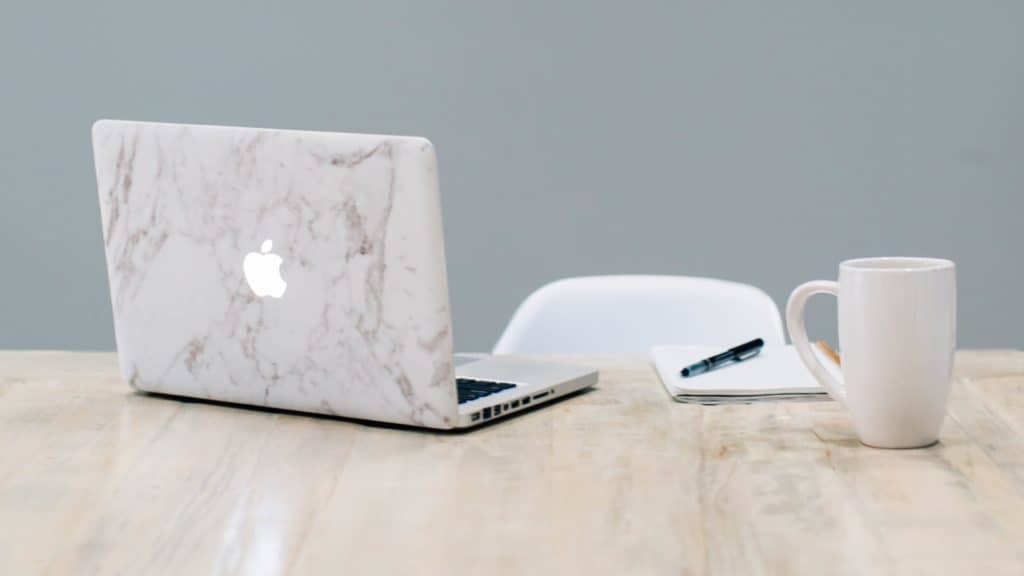 MacBook with marble cover design, pen on notepad and mug on table