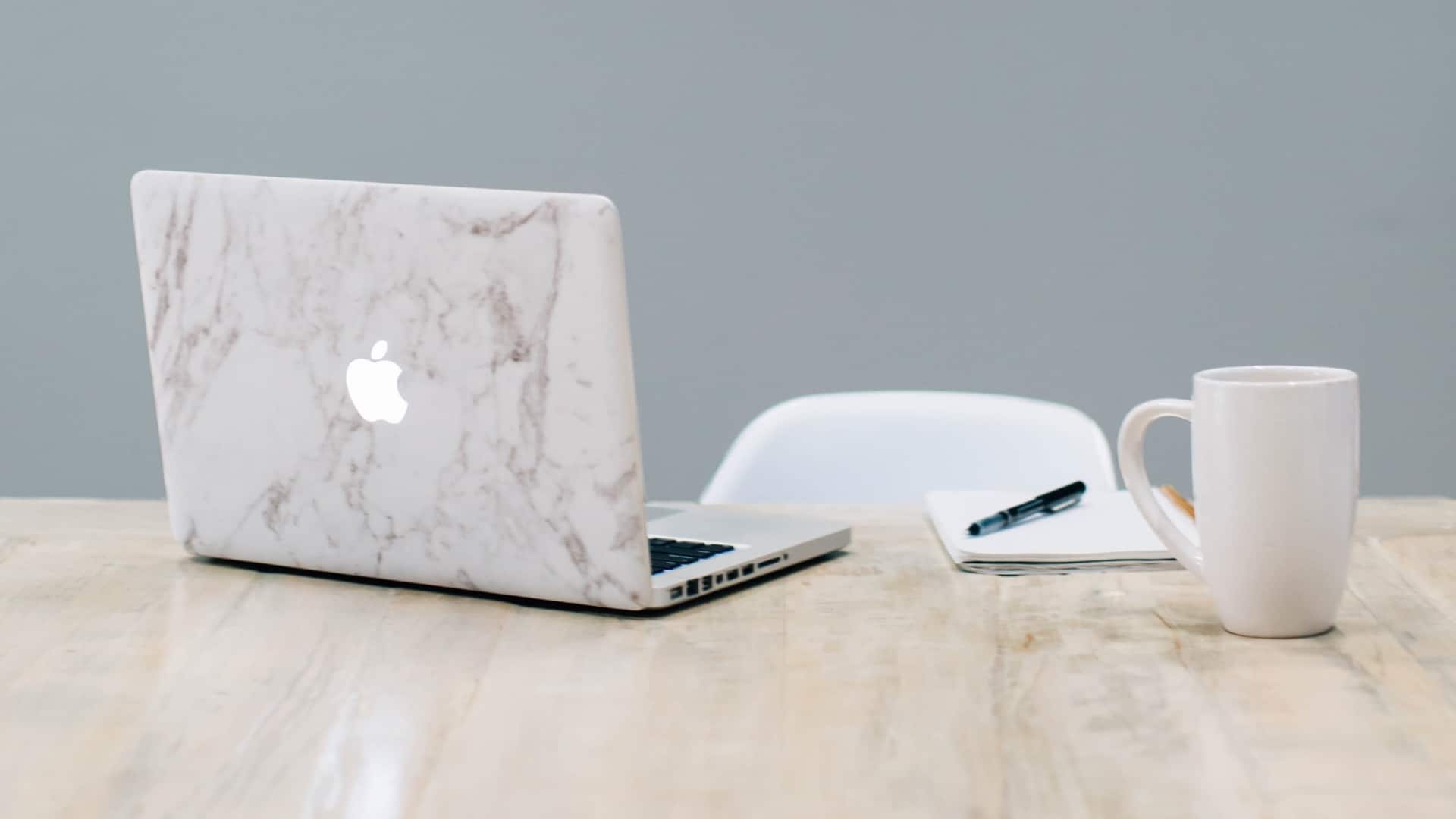 MacBook with marble cover design, pen on notepad and mug on table