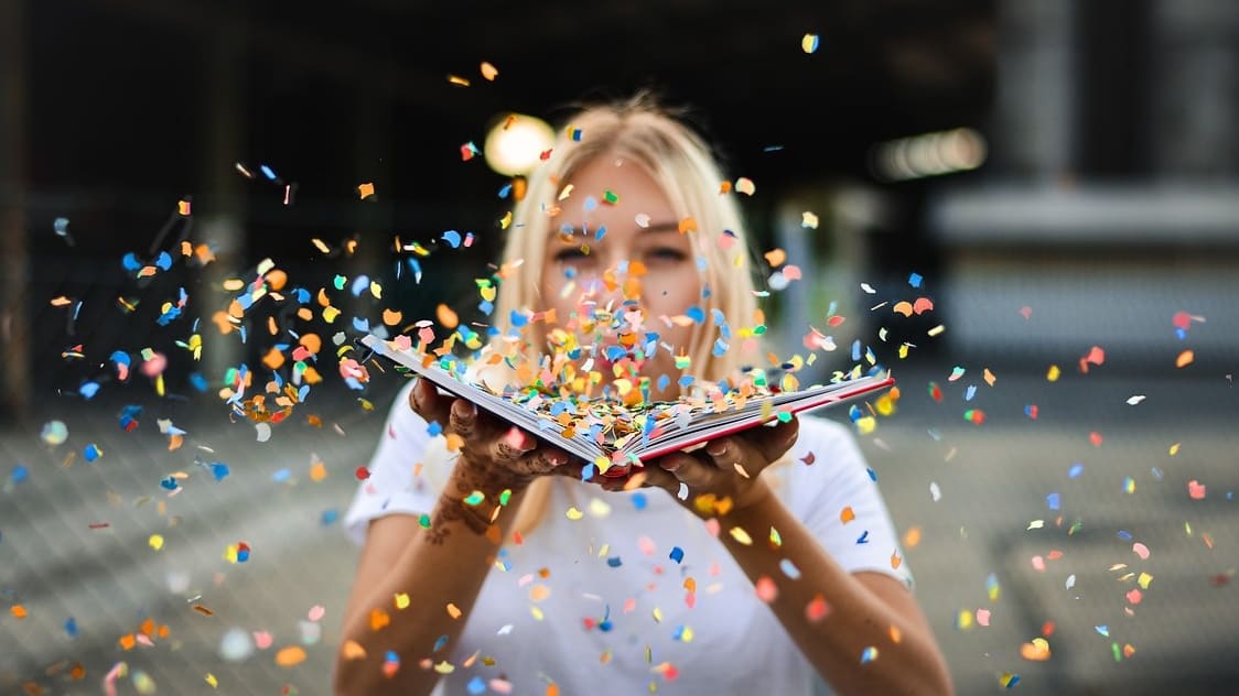 Woman blowing confetti off a book into the camera