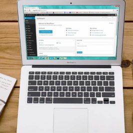 Open laptop with WordPress on screen, flanked by a notepad and pen, phone and cup of coffee