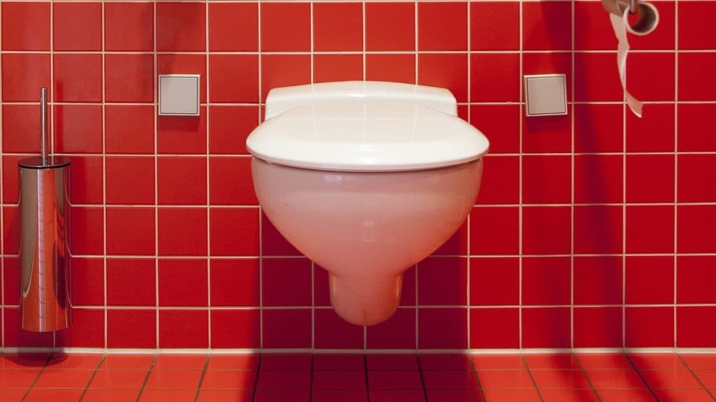 White toilet against a red tiled wall