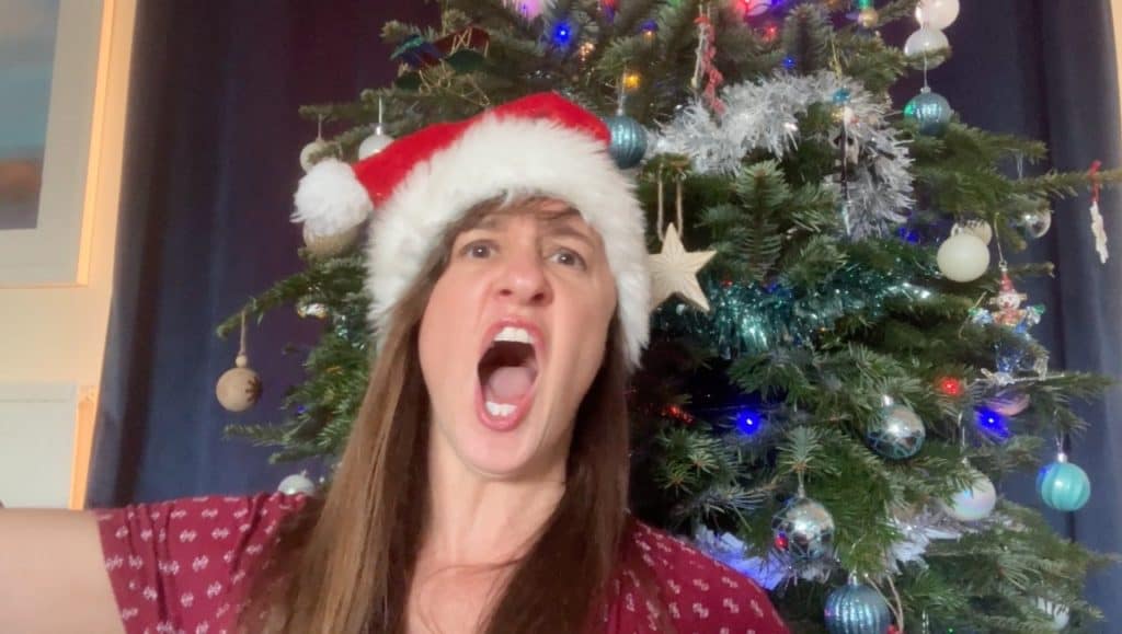 Debbie Emmitt in Santa hat, singing in front of Christmas tree