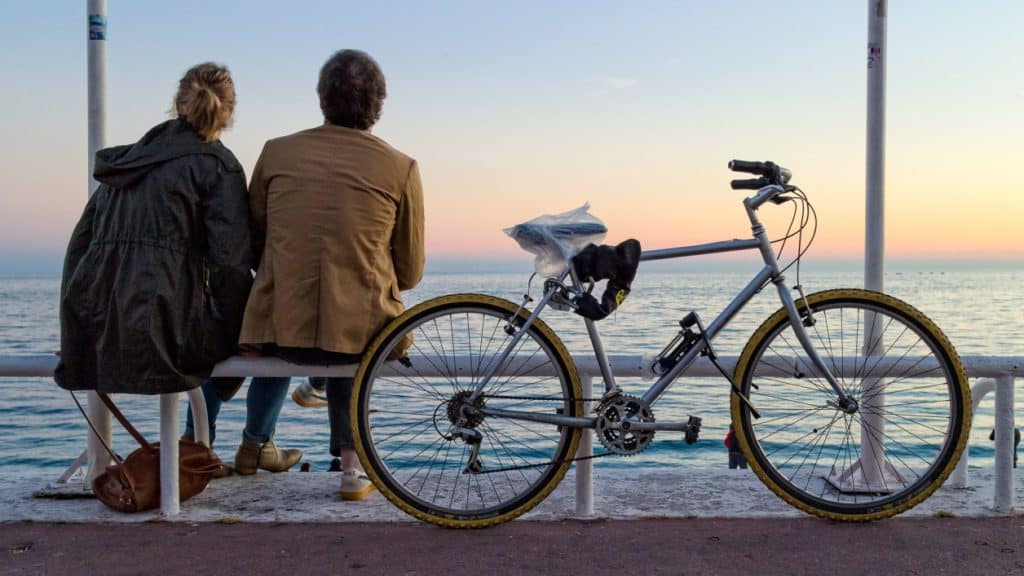 Man and woman sitting talking, looking at sea, bicycle nearby