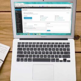 Open Macbook on wooden desk, WordPress on screen, with cup of coffee and notebook next to it