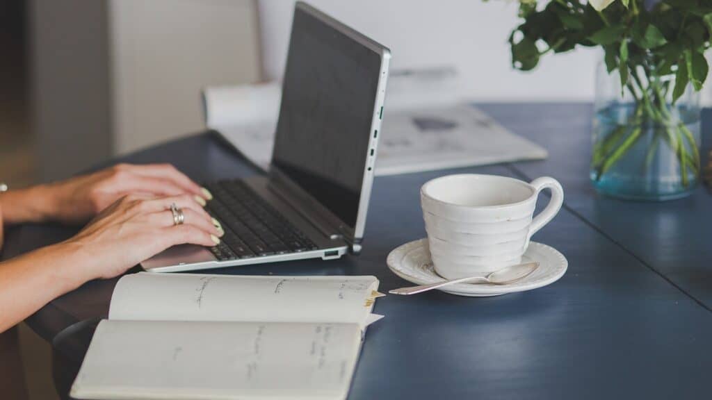 Hands typing on laptop, cup of coffee alongside