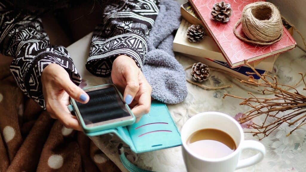 Woman's hands holding phone with cup of tea next to her