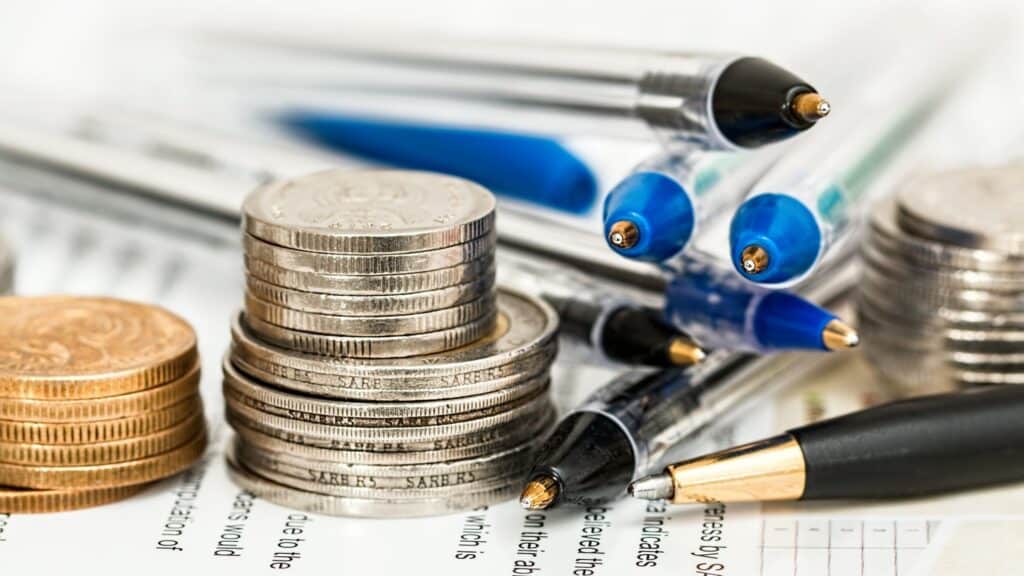 Black and blue biros with piles of coins on documents