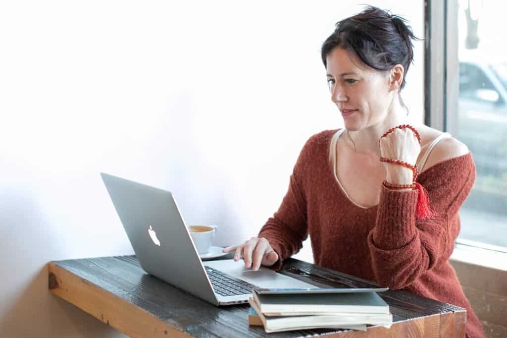 Woman with brown hair and red top smiling while looking at laptop