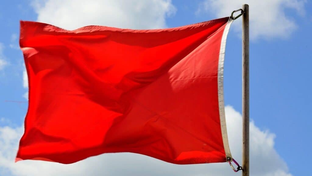 Red flag flying against a blue sky with white clouds