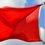 Red flag flying against a blue sky with white clouds