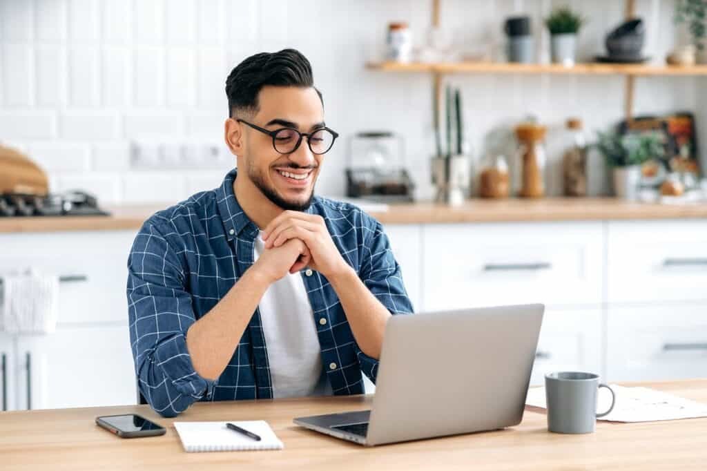 Young dark-haired man with beard smiling in front of laptop