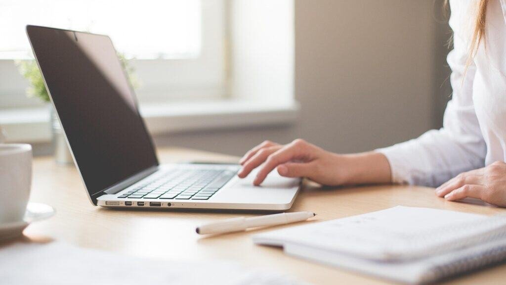 Close-up of woman's arm in a white blouse, her hand on a laptop