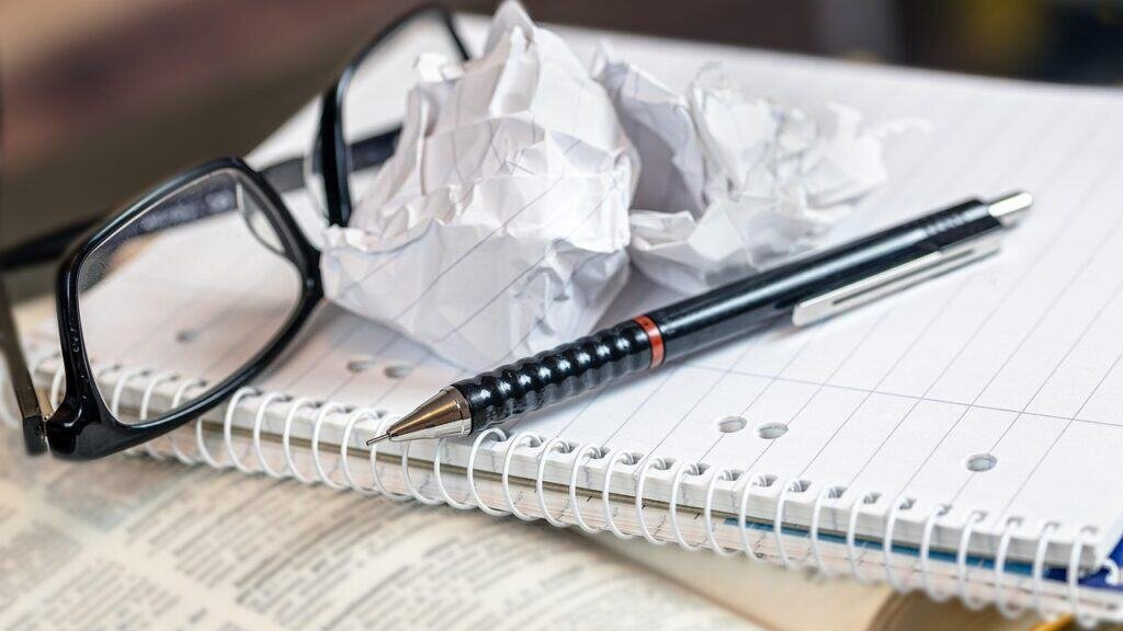 Screwed up ball of paper, glasses and pen on blank pad of paper